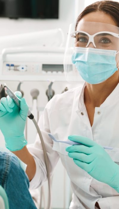 European mid pleased dentist woman in face mask working in dental clinic
