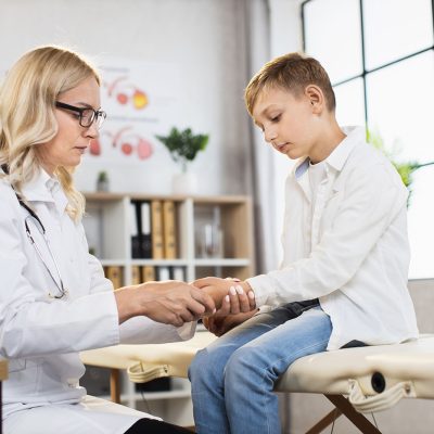 Teenage boy having medical consultation with competent doctor at modern clinic. Female physician examining male patient at own cabinet. Concept of health care.